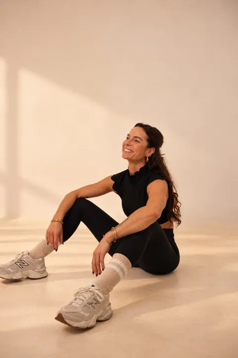 Lucile, assise au sol en tenue de sport noire, sourit.