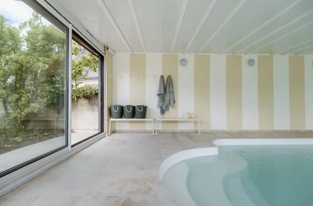 La piscine intérieure chauffée du pavillon, murs à rayures crème et baie vitrée ouverte sur la verdure.