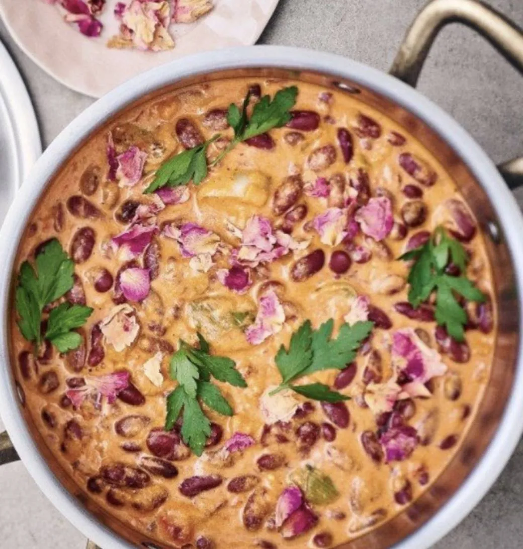 Plat mijoté de haricots rouges au lait de coco dans une sauteuse en cuivre, parsemé de persil plat et de pétales de rose.